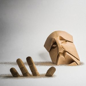 Origami of a man's head sinking with his hand outstretched and both dissolving in wind.
