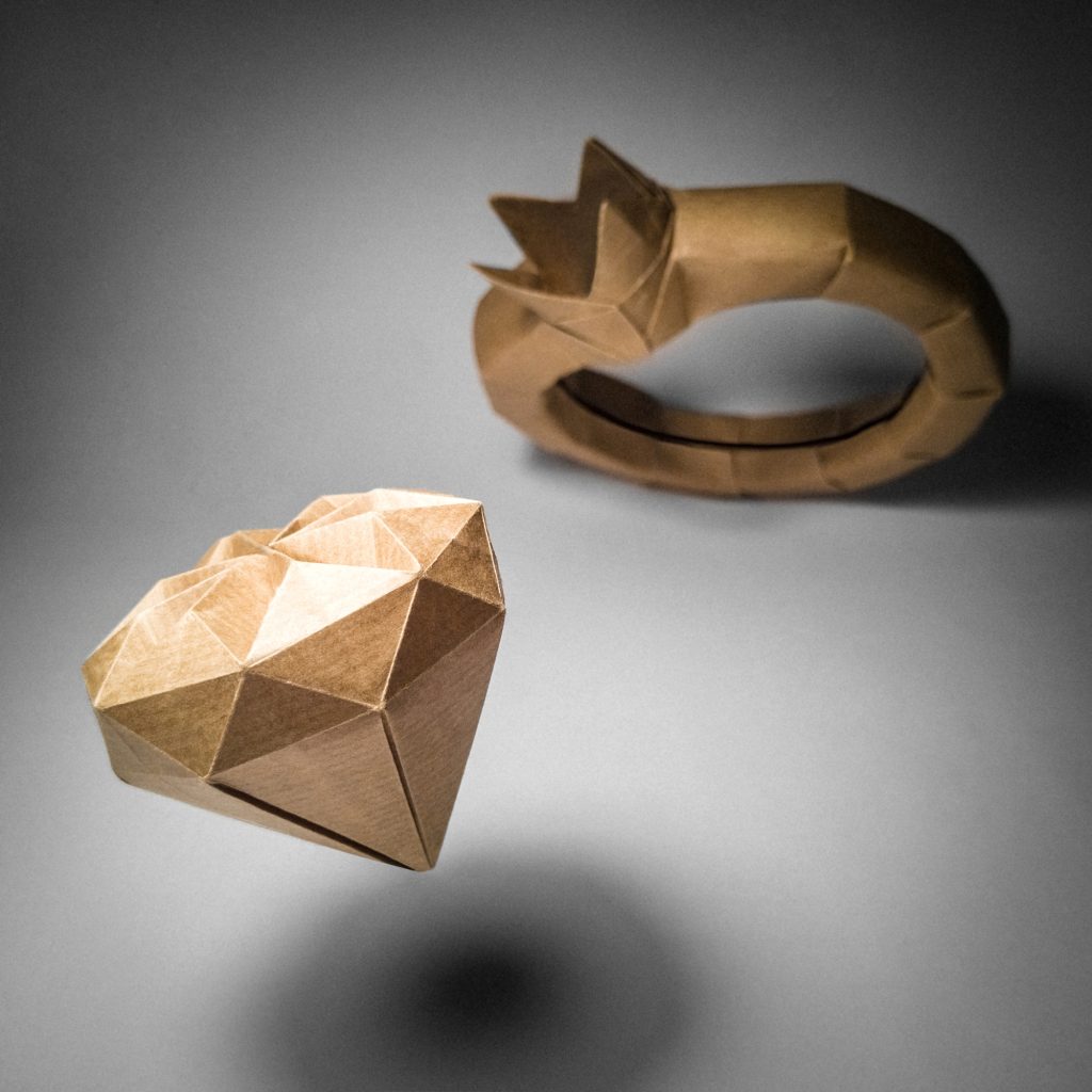 Origami of a diamond falling out of a wedding band to the floor.